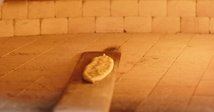 POV chef puts Turkish pide in stone oven. Fire burns in a stone oven in a restaurant's bakery. Baking traditional Turkish closed pide. Close-up, slow motion