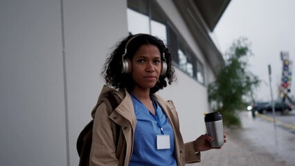 Female nurse, doctor going home from work, waiting for bus, listening music, drinking coffee and scrolling on smartphone. Work-life balance of healthcare worker as parent and partner. - Powered by Adobe