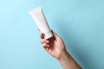 Woman with tube of hand cream on light blue background, closeup