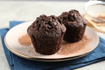 Delicious chocolate muffins and cacao powder on light grey table, closeup