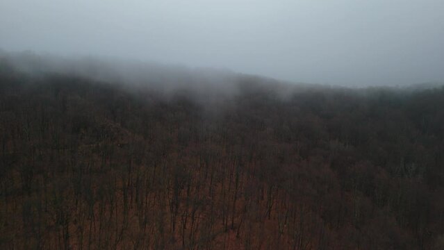 Drone of heavy fog over Pocono Mountain forest and green field behind it with snow and buildings