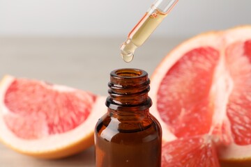 Dripping grapefruit essential oil from pipette into bottle and fresh fruit on table, closeup