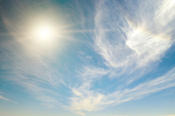 Bright sun on blue sky and cirrus clouds.