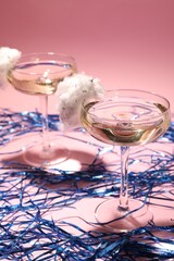 Tasty cocktails in glasses decorated with cotton candy and blue shiny streamers on pink background
