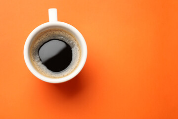 Fresh coffee in cup on orange background, top view. Space for text