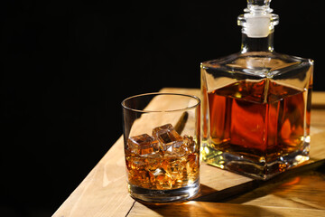 Whiskey with ice cubes in glass and bottle on wooden crate against black background, closeup. Space for text