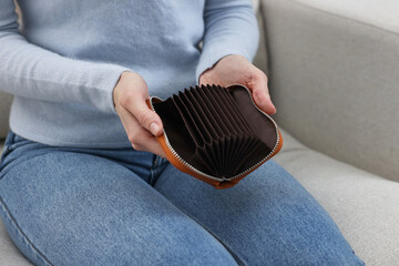 Woman with empty wallet on sofa indoors, closeup