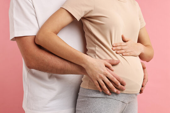 Man touching his pregnant wife's belly on pink background, closeup