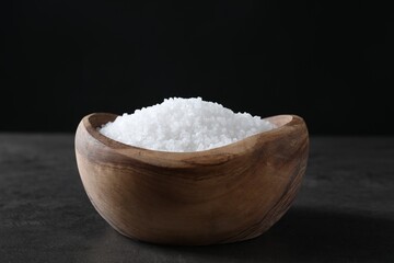 Natural salt in wooden bowl on dark grey table
