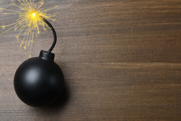 Old fashioned black bomb with lit fuse on wooden table, top view. Space for text
