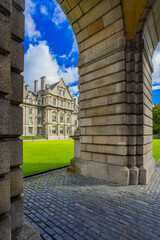 Trinity College Dublin, Ireland. The image features a view of the college through a stone archway, with cobblestones  in the foreground. The college's historic buildings are in the background