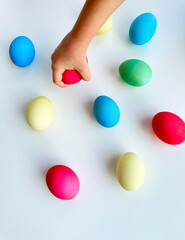 Child's hand picking up blue Easter egg among colorful eggs on white surface, interactive and engaging holiday activity concept. Can be used for educational content highlighting fine motor skills