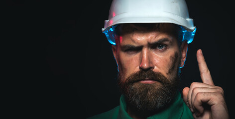 Closeup portrait of construction worker in hard hat pointing finger up. Bearded man protective...
