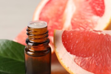 Grapefruit essential oil in bottle and fruit on table, closeup