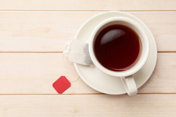 Tea bag and cup of hot beverage on light wooden table, top view