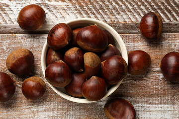 Sweet fresh edible chestnuts in bowl on wooden table, top view