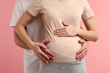 Man touching his pregnant wife's belly on pink background, closeup