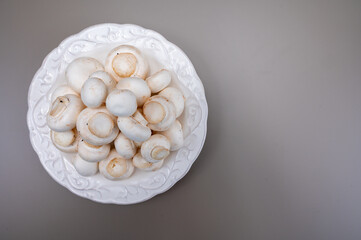 White champignon mushrooms fresh uncooked on white ceramic plate copy space