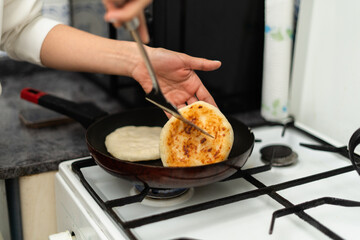 A person flipping golden-brown arepas in a frying pan, a traditional Colombian breakfast dish