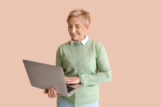 Mature female programmer working with laptop on beige background