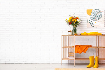 Shelving unit with bouquet of autumn flowers, umbrella and rubber boots near white brick wall