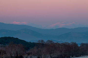 A river in Thessaly and the snowy peaks of Olympus mountain in Greece. Pink sky in winter time. Sunset time.