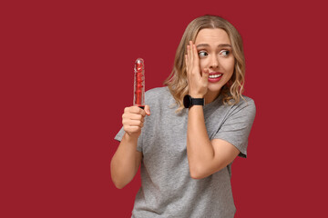 Ashamed young woman with vibrator on red background