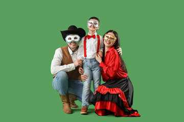 Happy family in costumes and carnival masks on green background