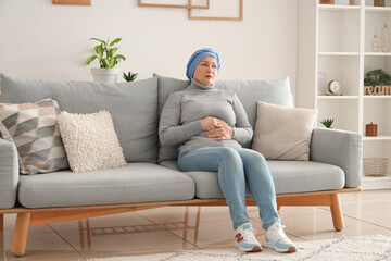 Mature woman after chemotherapy sitting on sofa at home. Stomach cancer concept