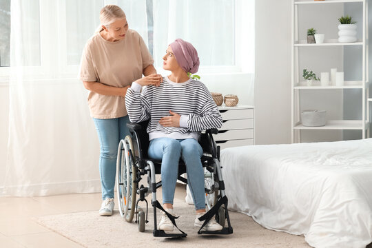 Young woman after chemotherapy in wheelchair with her mother at home. Stomach cancer concept