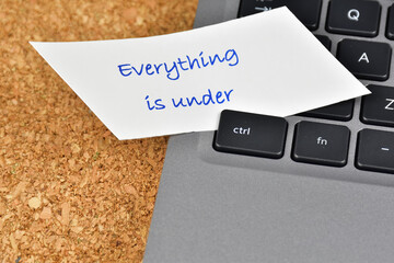 Everything is under control concept. Laptop keyboard with everything is under words on a white paper under the control key.