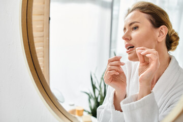 appealing blonde woman with collected hair in bathrobe cleaning her teeth with dental floss