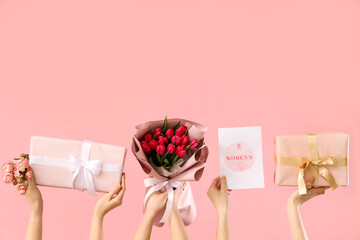 Female hands with bouquet of tulips, gift boxes and festive postcard on pink background. Shopping...