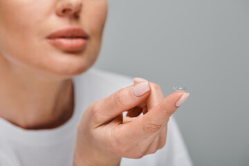 Naklejka premium cropped view of concentrated female model wearing contact lenses carefully on gray background