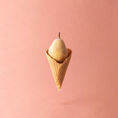 Frozen pear in ice cream cone on pink pastel background. Fruit creative concept.