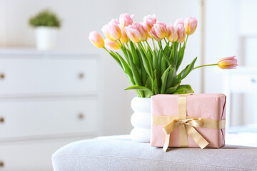 Vase with tulips and gift box for International Women's Day on soft bench in bedroom, closeup