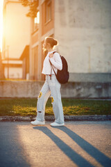 A beautiful European teenager, captured in a side-profile portrait, walks home during sunset after school, carrying her backpack