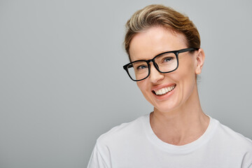 cheerful attractive woman with blonde hair with glasses smiling happily at camera on gray background