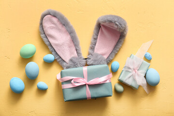 Bunny ears with Easter eggs and gift boxes on yellow background