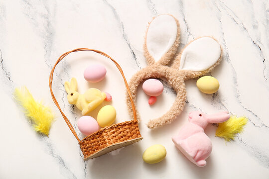 Bunny ears with Easter eggs and wicker basket on white marble background