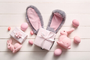 Bunny ears with Easter eggs and gift boxes on white wooden background