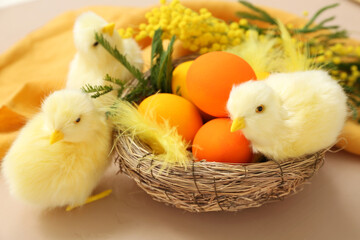 Easter eggs in nest and chickens on beige table