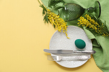 Beautiful Easter table setting with painted egg, green napkin and mimosa on yellow background