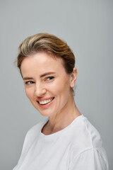 jolly attractive woman with blonde hair and contact lenses posing on gray backdrop and looking away