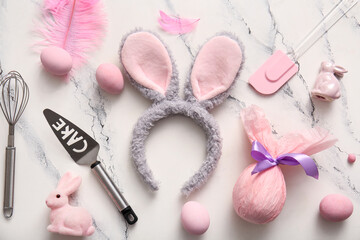 Bunny ears with Easter eggs and cooking utensils on white marble background
