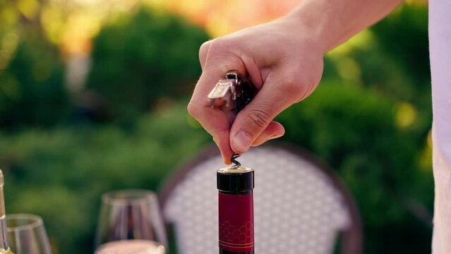 Close-up of a male sommelier's hand using a corkscrew to unscrew the wooden cork of wine bottle