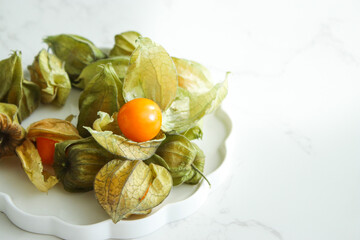 Ripe physalis fruits on white plate and marble table