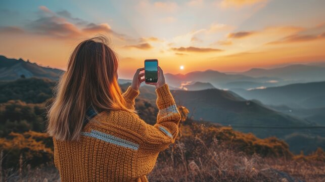 Anonymous female traveler in casual sweater taking picture of amazing landscape with mountains and sunset sky on smartphone during vacation