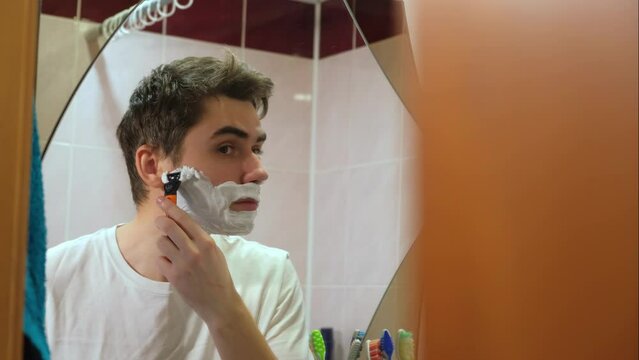 a man takes care of his beard, a guy applies shaving foam, a man shaves in front of a bathroom mirror