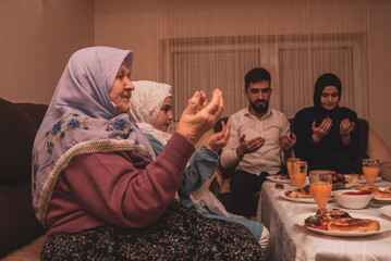 Muslim family together making iftar dua to break fasting during Ramadan dining table at home young...